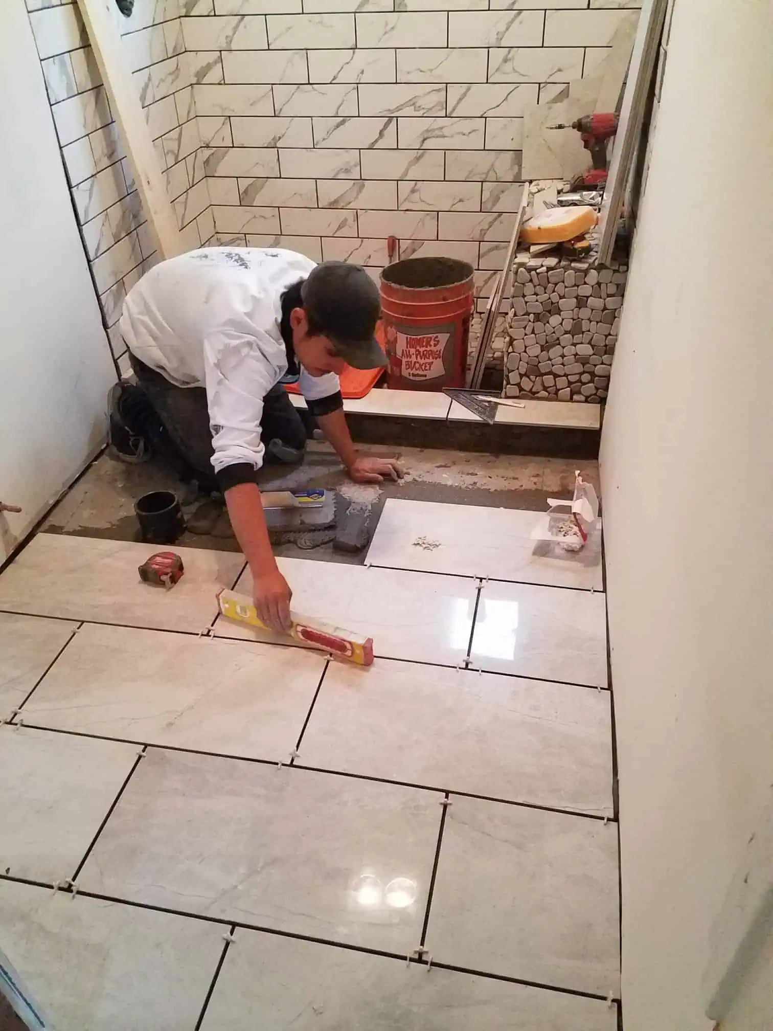 Worker installing large ceramic tiles in a bathroom renovation project.