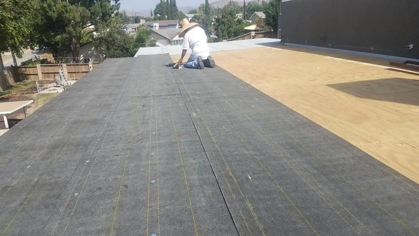 Roof construction with worker installing roofing underlay on a flat roof.