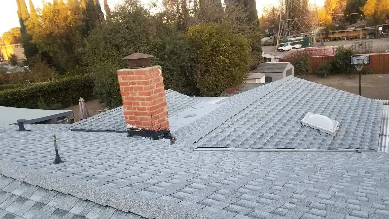 Residential roof with chimney, skylight, and asphalt shingles in a suburban neighborhood.