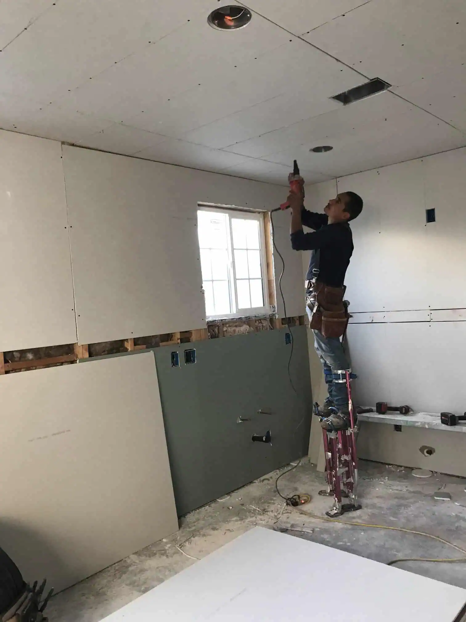 Worker installing drywall ceiling in a home renovation project.